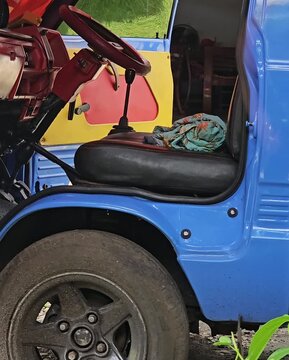 Close up view of the driver seat and red steering wheel of a modified blue mini truck with an orange tarpaulin roof