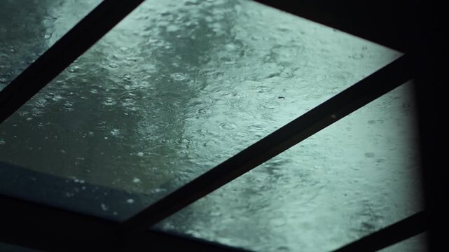 Close up of raindrops falling on transparent glass roof during heavy rain, abstract wet raindrop ripples on glass window background for monsoon season, stormy weather, cozy stay home.