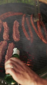 Person grilling sausages and cevapi on barbecue