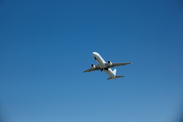 Obraz premium White passenger airplane taking off and gaining altitude against a blue sky