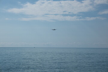 Naklejka premium White passenger plane descending for landing over the sea against a cloudy blue sky