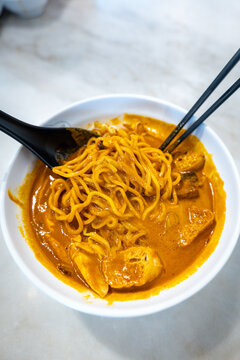Ipoh curry mee noodles being lifted with chopsticks from rich coconut curry broth.