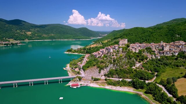 Castel di Tora Turano lake drone view. Cinematic aerial flyover of bridge beautiful medieval hilltop village in Rieti Italy. Emerald turquoise water island scenic landscape travel destination