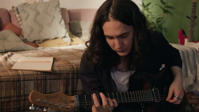 Young man playing electric guitar in bedroom, then writing lyrics in notebook. Footage for ads promoting music education, creative hobbies, or songwriting apps