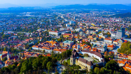 Fototapeta premium Aerial view of Ljubljana Castle on its wooded hill above the old town with the city and Alpine foothills, Slovenia