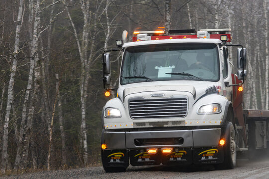 Parents, Quebec, 19 May 2026 : A white Freightliner commercial truck with amber warning lights drives on a gravel road through a forest.