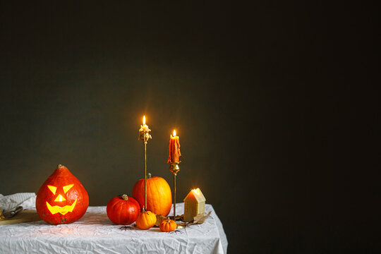 Glowing jack o lantern, carved pumpkins, spooky spiders and burning candles on dark moody background. Happy Halloween. Atmospheric Halloween preparation and decorations, space for text