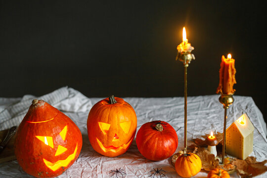 Glowing jack o lantern, carved pumpkins, spooky spiders and burning candles on dark moody background. Happy Halloween. Atmospheric Halloween preparation and decorations, space for text