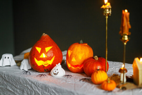 Happy Halloween. Carved halloween pumpkins with burning candles and spiders on table against dark background. Atmospheric halloween decorations, holiday banner