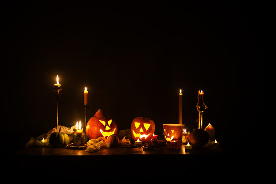 Happy Halloween. Jack o lantern glowing pumpkins, spooky spiders and burning candles on dark moody background. Spooky atmospheric halloween night, space for text. Trick or treat