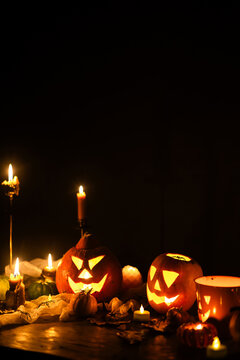 Happy Halloween. Jack o lantern glowing pumpkins, spooky spiders and burning candles on dark moody background. Spooky atmospheric halloween night, space for text. Trick or treat