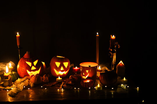 Jack o lantern glowing pumpkins, spooky spiders and burning candles on dark moody background. Happy Halloween. Spooky atmospheric halloween night, space for text. Trick or treat