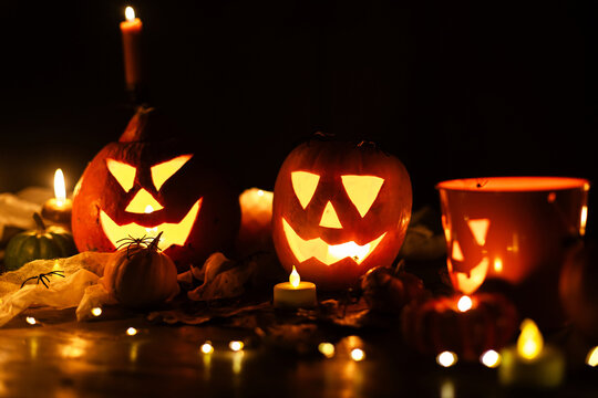 Happy Halloween. Jack o lantern glowing pumpkins, spooky spiders and burning candles on dark moody background. Spooky atmospheric halloween night, space for text. Trick or treat