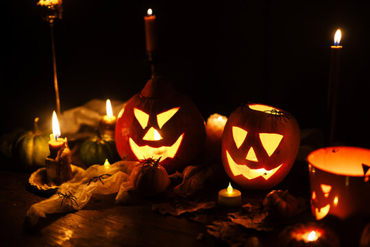 Jack o lantern glowing pumpkins, spooky spiders and burning candles on dark moody background. Happy Halloween. Spooky atmospheric halloween night, space for text. Trick or treat