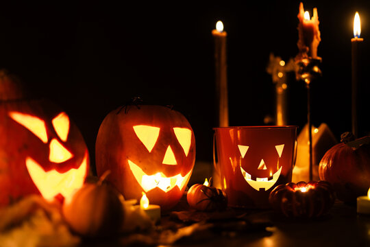 Jack o lantern glowing pumpkins, spooky spiders and burning candles on dark moody background. Happy Halloween. Spooky atmospheric halloween night, space for text. Trick or treat