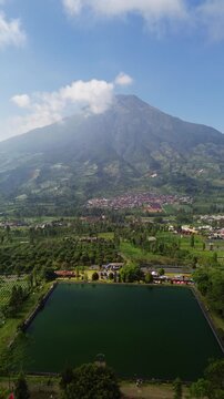 Aerial drone footage of Embung Kledung, a scenic artificial reservoir in Temanggung, Central Java, Indonesia, surrounded by the majestic Mount Sindoro and Mount Sumbing.