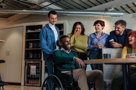 Diverse colleagues a disabled person sharing a laugh in modern office break room
