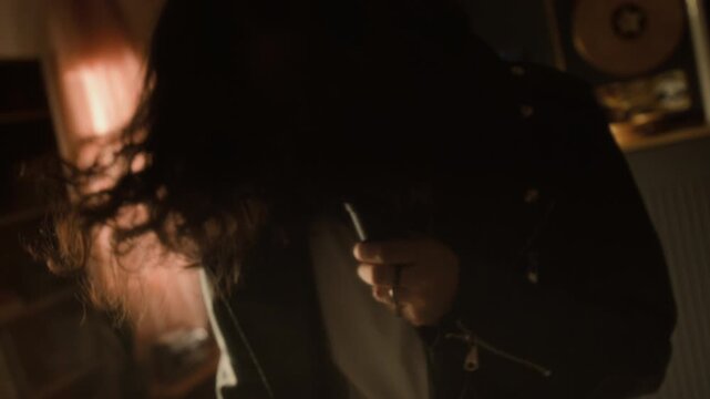 Young vocalist with curly hair wearing leather jacket singing passionately into microphone and headbanging in home studio. Clip for music, hobby, and creative lifestyle promos