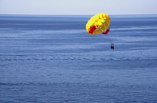 Yellow parachute with people flying over deep blue ocean