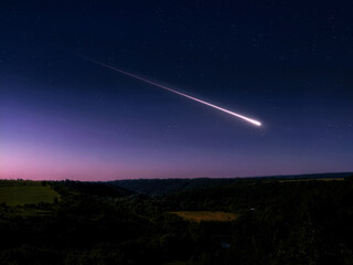 Bright meteor trail in the starry sky at dawn. Astronomical landscape with fireball over the hills. © Nazarii