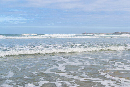 Calming ocean waves gently roll onto the sandy shore under a vast cloudy sky. With nobody around, this serene seascape evokes deep peace, perfect for mindfulness and wellness designs.