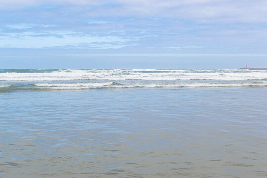 A tranquil coastal view of gentle ocean waves crashing on a sandy beach under a soft blue sky. This serene scene evokes peace and calm. Perfect for travel or wellness designs. Nobody.