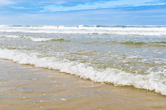 Beautiful ocean waves roll onto a serene sandy beach under a bright blue sky, evoking a peaceful, relaxing summer holiday vibe. Perfect coastal background with nobody around.