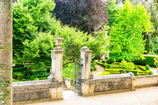 An elegant stone gateway with an ornate iron gate opens into a lush, manicured historic garden, perfect for themes of discovery, elegance, romance, and classic landscape design.