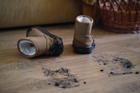 Dirty boots placed on a wooden floor in a messy and neglected interior room with a close-up, ground-level perspective. Home care and cleaning routine.
