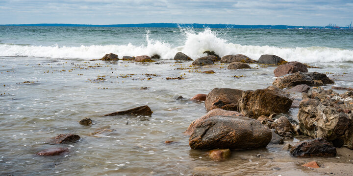Rocky east coast of denmark with view the port of aarhus on horizon with crashing waves. 