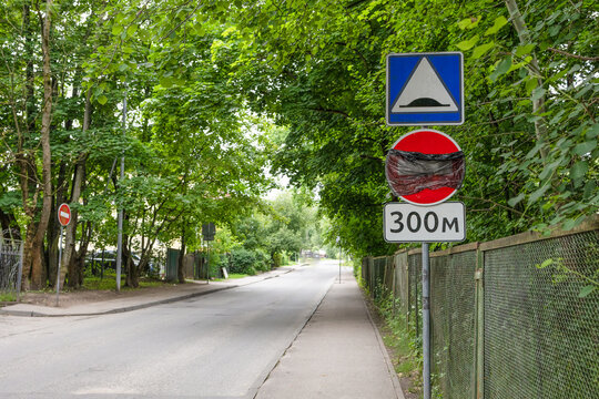 Collection of traffic signs including a speed bump warning and road restriction sign installed along a tree-lined urban road. Suitable for transportation, traffic regulations, road safety and