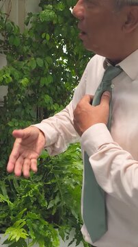 senior asian businessman sweating in summer heat, waving his hand and shirt to cool down outdoors during hot day, vertical vdo
