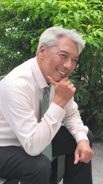 Old aged, senior business man thinking, planning with happy positive optimistic facial expression, green city outdoor scene, vertical video