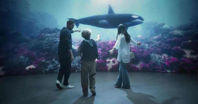 Happy Family of Three in Oceanarium Marine Mammal Park. Young Child Points Excitedly at a Passing Orca While Mom and Dad Watch in Wonder, Learning About Marine Life Together. Static Shot