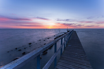 Obraz premium Landscape photograph of a wooden pier stretching into Markermeer near Volendam in North Holland, Netherlands, during a peaceful sunrise. The first light of day paints the sky in soft shades.