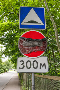 Collection of traffic signs including a speed bump warning and road restriction sign installed along a tree-lined urban road. Suitable for transportation, traffic regulations, road safety and