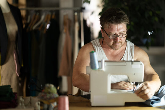 Middle-aged male dressmaker working with sewing-machine at night