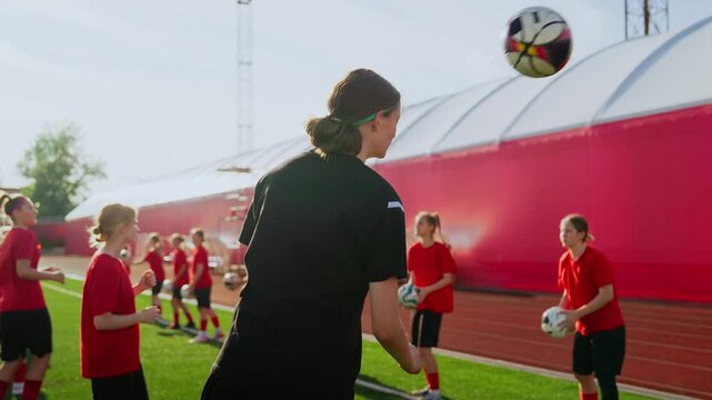 Focused womens soccer team training drills on sunny outdoor field, teenage players practicing ball control, coordination, and teamwork under coach supervision