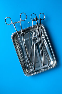 Sterile surgical instruments and tools - scalpels, scissors and others - in a stainless tray on blue background, top view