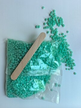 Green hard wax beads spilled from plastic bag with wooden spatula on white background hair removal concept