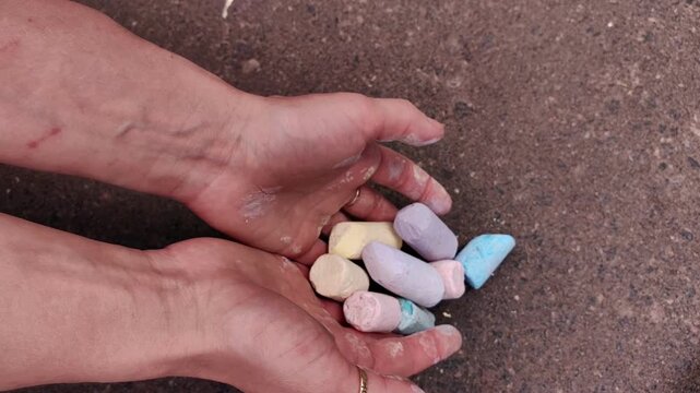 Adult holding several colorful sidewalk chalk pieces in both hands, creative supplies, outdoor art, summer hobby, playful inspiration.