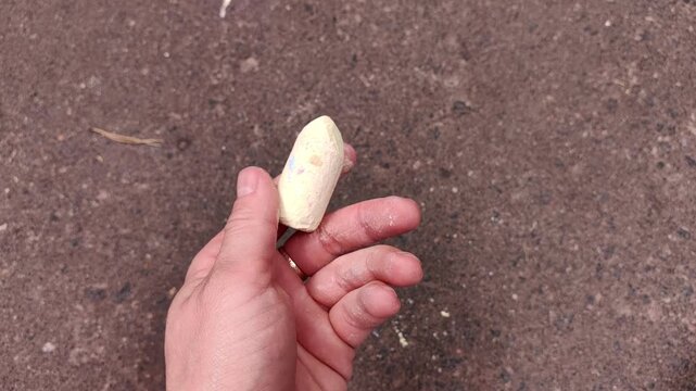 Adult holding a piece of white sidewalk chalk, close up of drawing tool, outdoor creativity, summer art, educational activity.