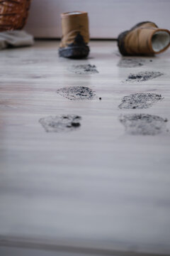 Footprints lead across a wooden floor next to old boots and a rolled blanket on the gray floor. The scene shows a relaxed indoor space with personal items scattered around.