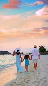 Rear view of an elegant family walking on a tropical paradise beach in the Maldives islands during sunset time