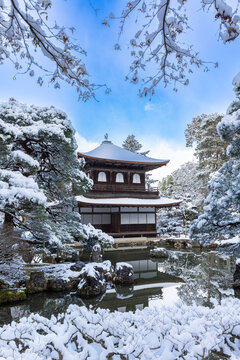 Stunning vertical view of a historic Japanese temple pavilion reflected in a pond surrounded by snow-covered trees, Kyoto.
