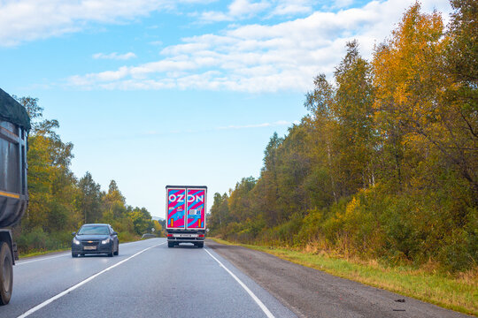 A cargo truck ozon and a passenger car driving on a highway lined with colorful autumn trees. vehicle traffic flow, commercial delivery shipping. Russia, Samara Oblast, September 13, 2025