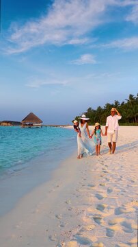 A happy family on summer holidays walks down a tropical paradise beach in the Maldives islands during sunset time<