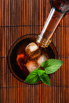 Chinotto soft drink with ice and fresh mint in glass on dark wooden background