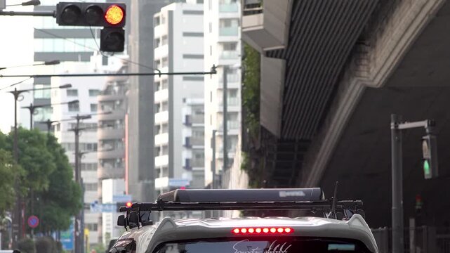 Cars waiting at a red light while pedestrians cross a busy Tokyo street