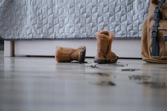 Muddy footprints on laminate floor with dirty children's boots indoors. Rainy day home cleaning concept